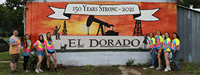EHS students and art teachers standing next to the completed mural of an oil derrick, oil pump and the El Dorado sign and a banner that says "150 years strong - 2021"