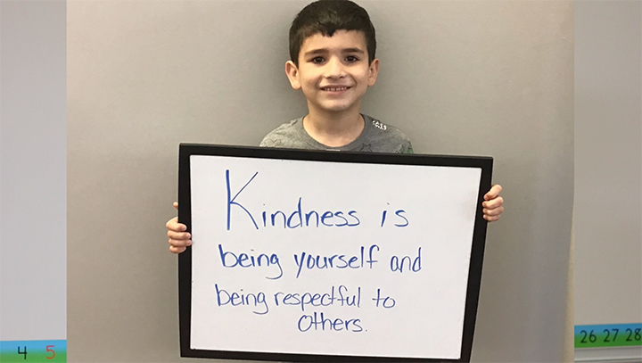 Student holding a sign that says, "Kindness is being yourself and being respectful to others."