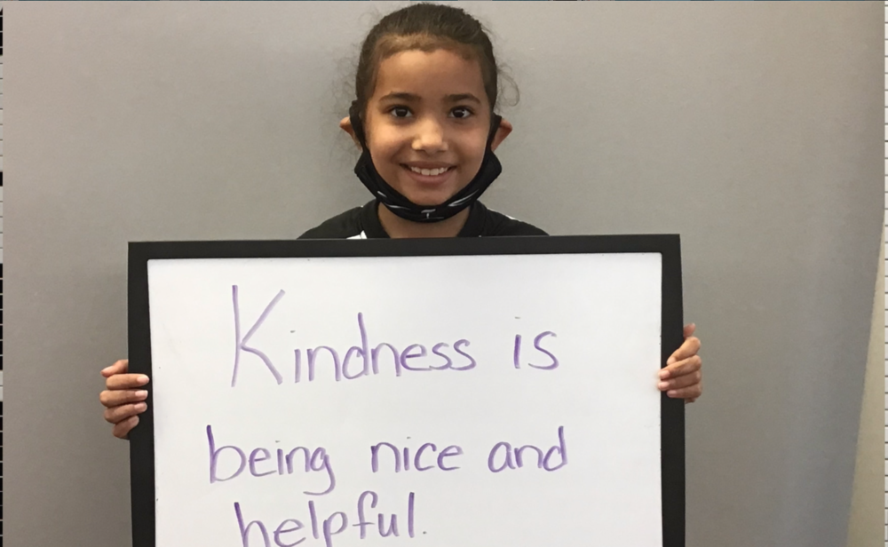 student holding a sign that says, "Kindness is being kind and helpful"
